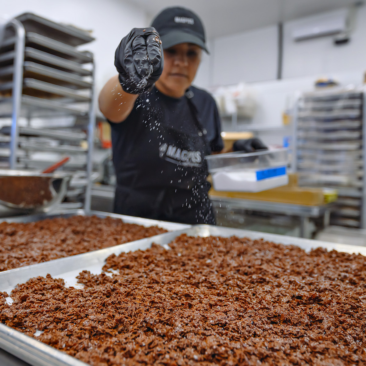 Pastry chef sprinkling salt on a sheet pan of chocolate wafers